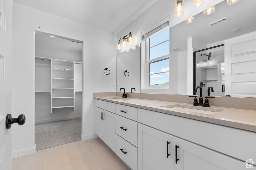 Full bath with double vanity, tile patterned floors, baseboards, and a shower with shower door