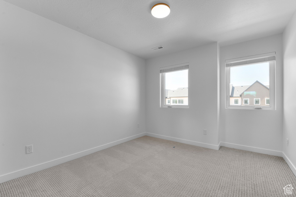 Unfurnished room featuring baseboards, light carpet, and a textured ceiling