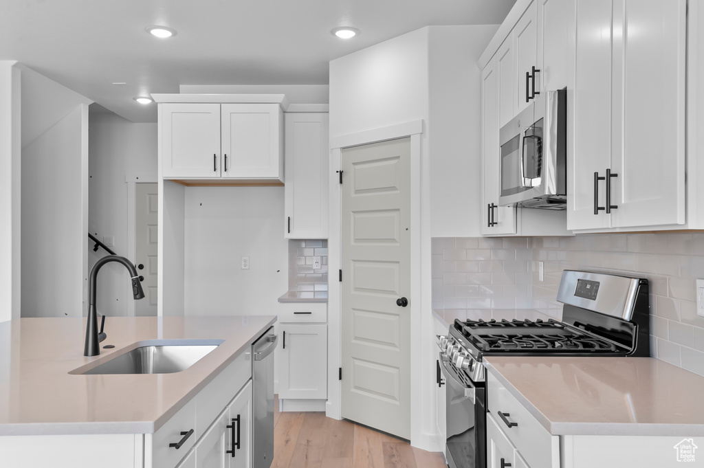 Kitchen featuring stainless steel appliances, a sink, light wood-type flooring, light countertops, and white cabinetry