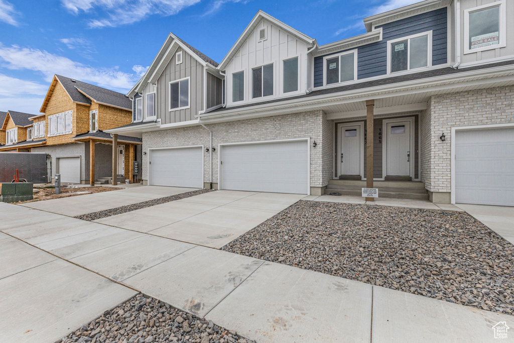 View of property featuring board and batten siding, an attached garage, concrete driveway, and brick siding
