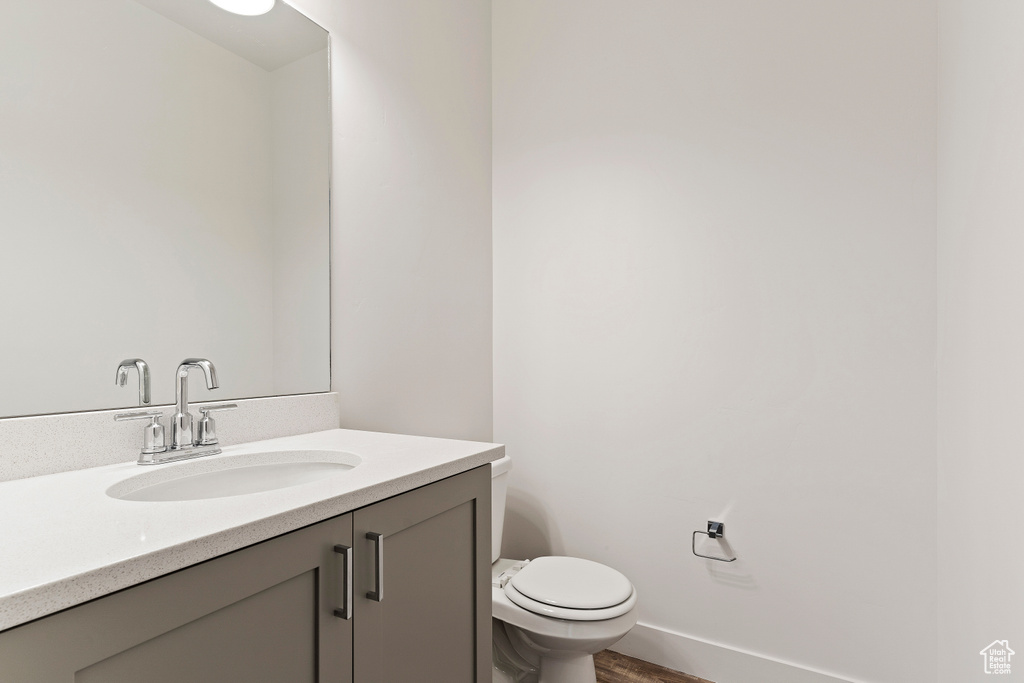 Bathroom featuring toilet, vanity, wood finished floors, and baseboards