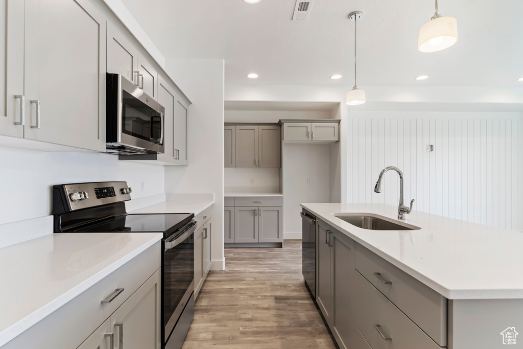 Kitchen with appliances with stainless steel finishes, gray cabinetry, a sink, light wood-style flooring, and pendant lighting