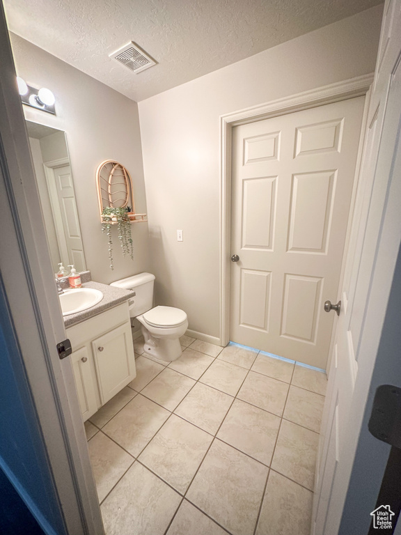 Half bath with tile patterned flooring, toilet, vanity, and a textured ceiling