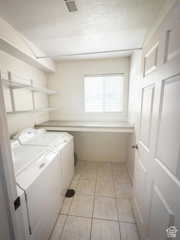 Laundry area featuring washer and dryer, a textured ceiling, and light tile patterned flooring