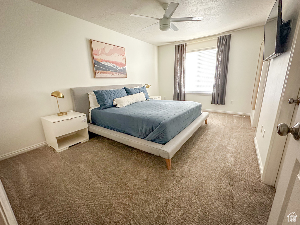 Bedroom with light carpet, a textured ceiling, baseboards, and a ceiling fan