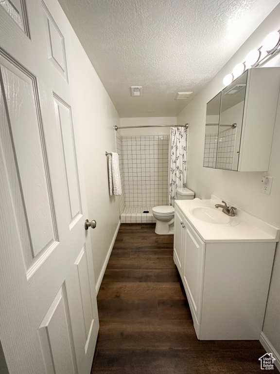 Full bathroom with a textured ceiling, curtained shower, wood finished floors, toilet, and vanity