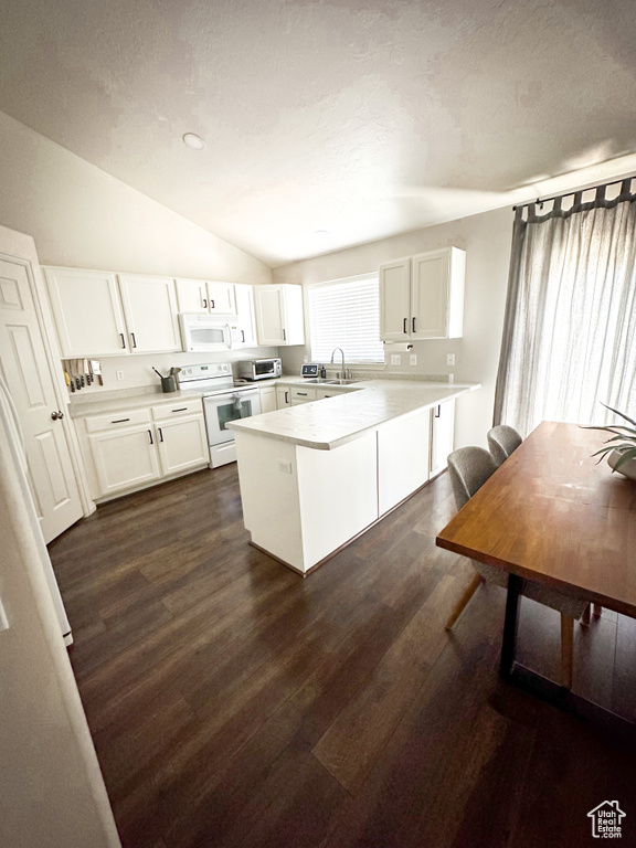 Kitchen featuring white appliances, vaulted ceiling, a peninsula, white cabinetry, and dark wood-type flooring
