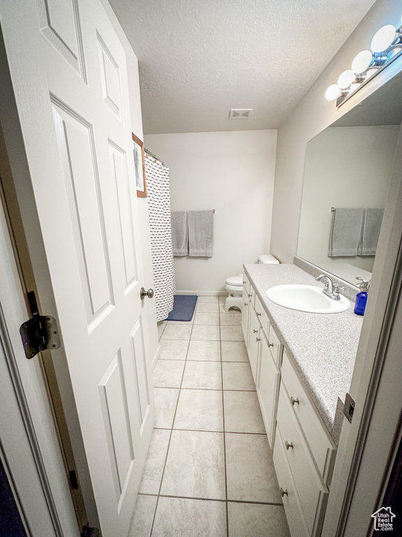 Full bathroom featuring a textured ceiling, vanity, toilet, tile patterned floors, and baseboards