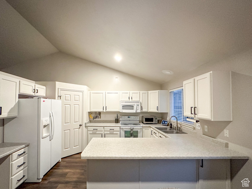 Kitchen featuring white appliances, lofted ceiling, a sink, a peninsula, and dark wood-type flooring