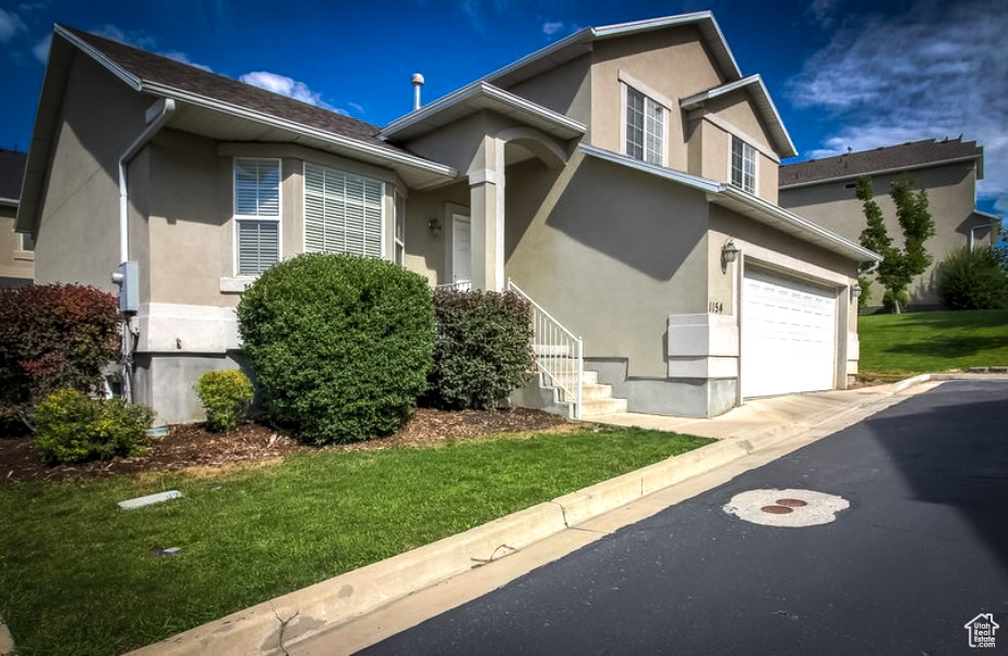 View of front facade featuring stucco siding, a front lawn, a garage, and driveway