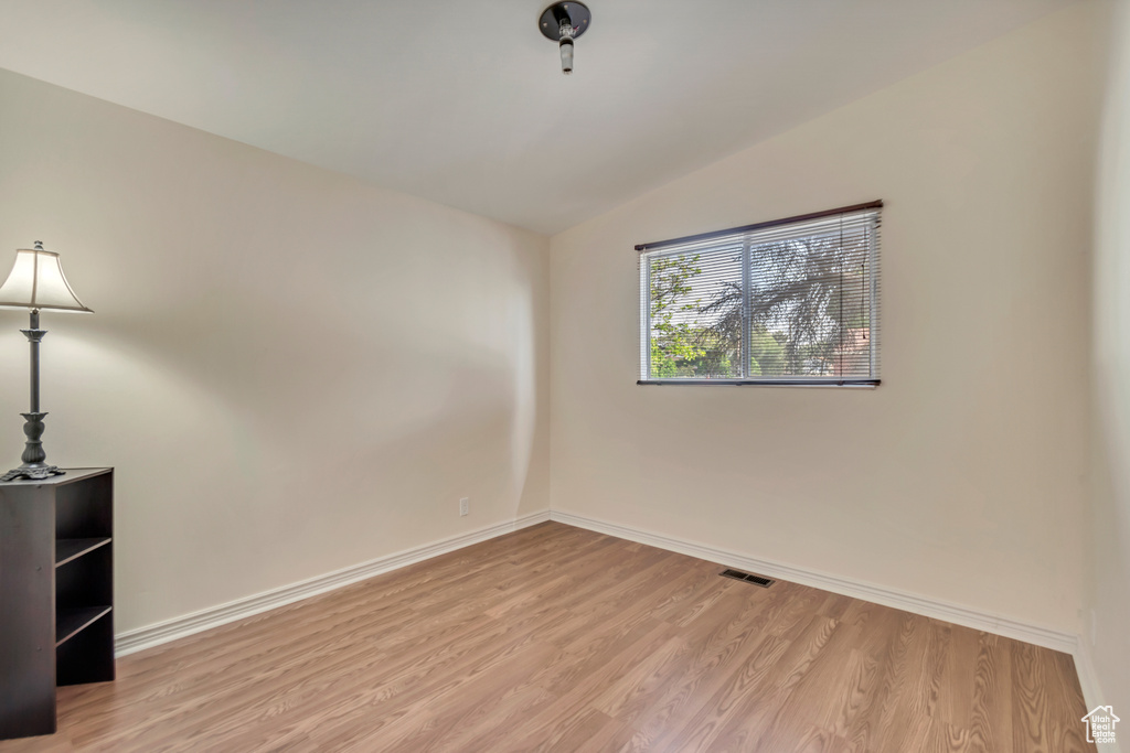 Empty room featuring lofted ceiling, wood finished floors, and baseboards