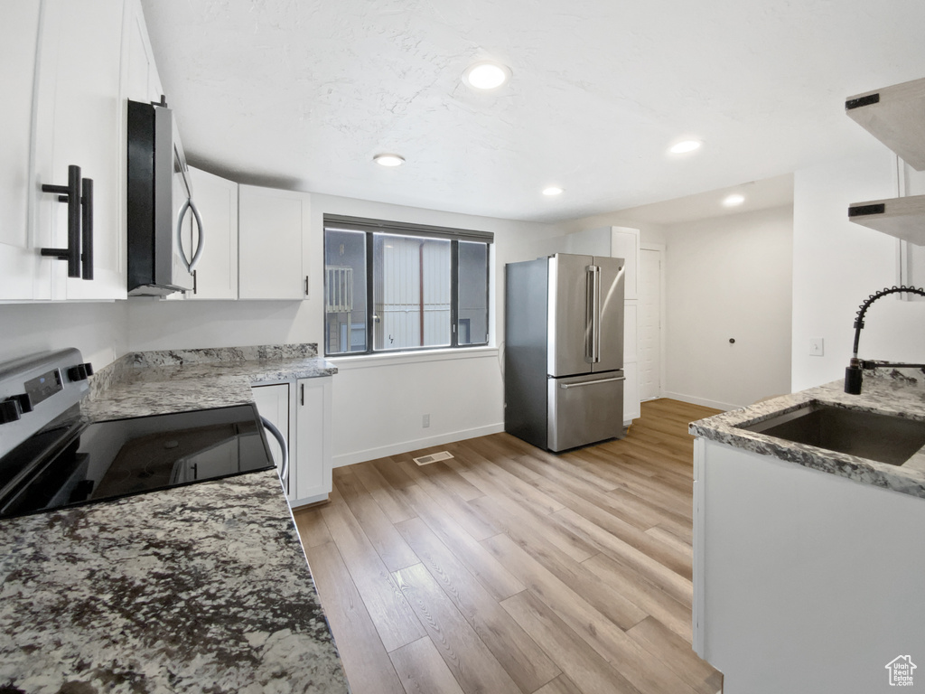 Kitchen with stainless steel appliances, a sink, light stone countertops, white cabinetry, and baseboards