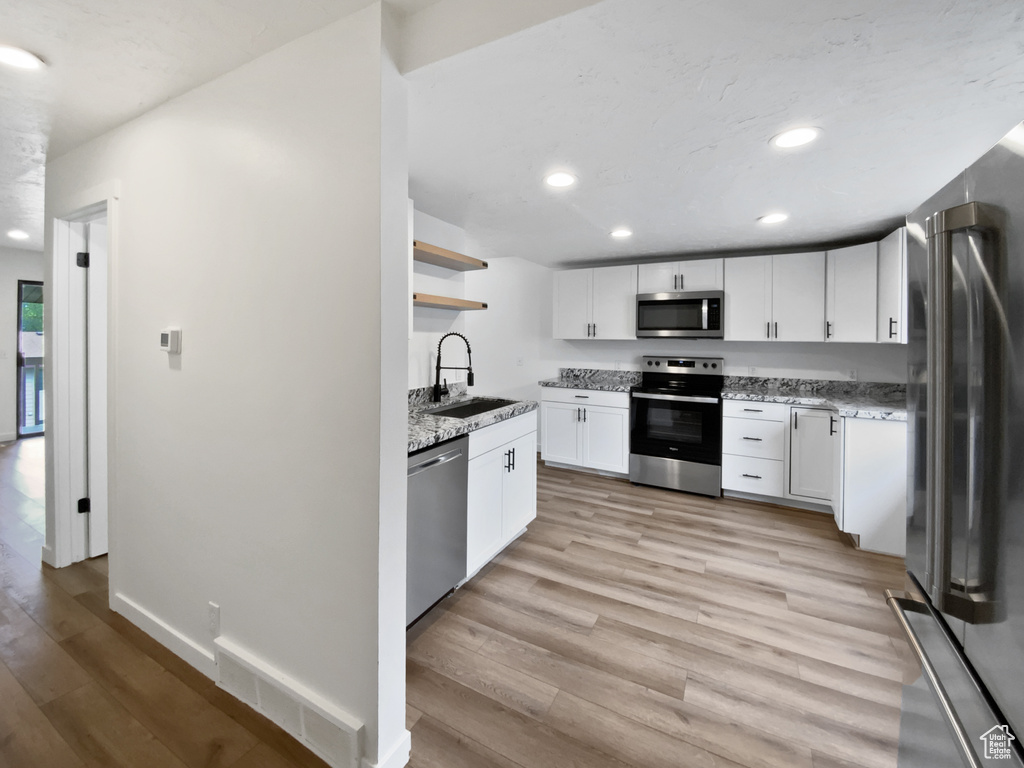 Kitchen with appliances with stainless steel finishes, a sink, open shelves, recessed lighting, and light wood-style floors