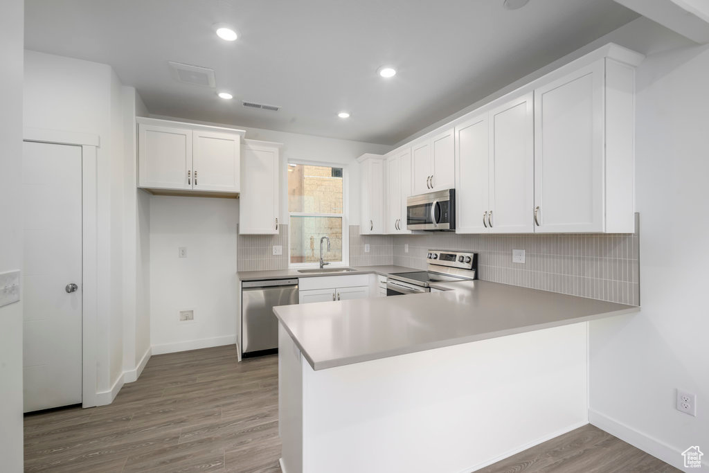 Kitchen featuring appliances with stainless steel finishes, a sink, wood finished floors, a peninsula, and baseboards