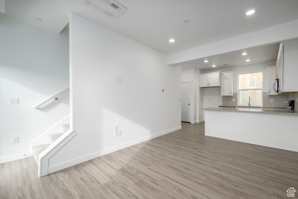 Kitchen featuring light wood-type flooring, stainless steel microwave, recessed lighting, white cabinetry, and a peninsula