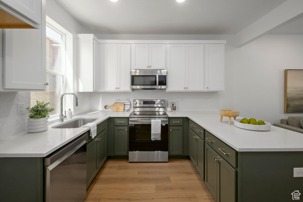 Kitchen with a sink, a peninsula, white cabinets, green cabinets, and appliances with stainless steel finishes