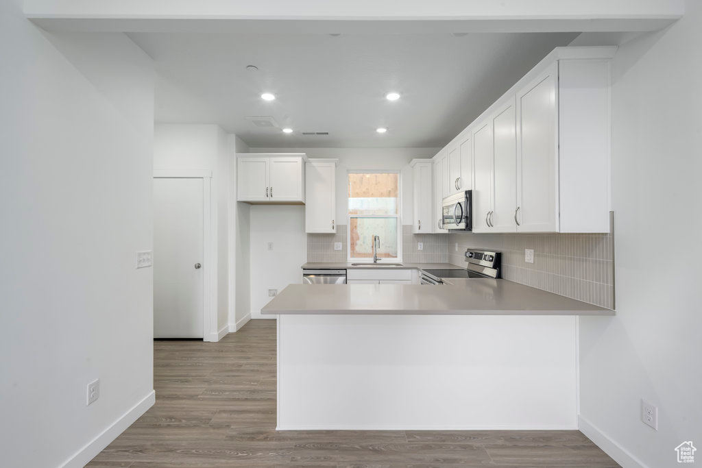 Kitchen featuring appliances with stainless steel finishes, a sink, a peninsula, backsplash, and recessed lighting