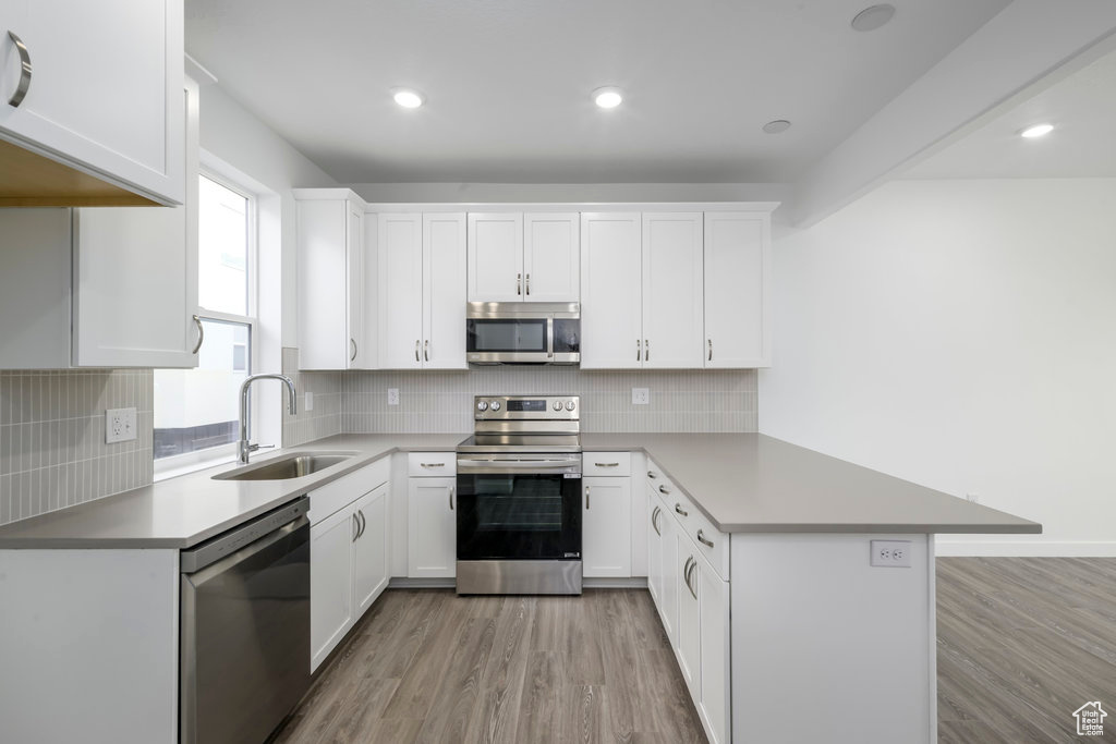 Kitchen featuring appliances with stainless steel finishes, a sink, a peninsula, light wood-type flooring, and white cabinets