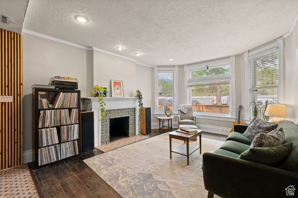 Living room featuring a fireplace, crown molding, plenty of natural light, a textured ceiling, and wood finished floors