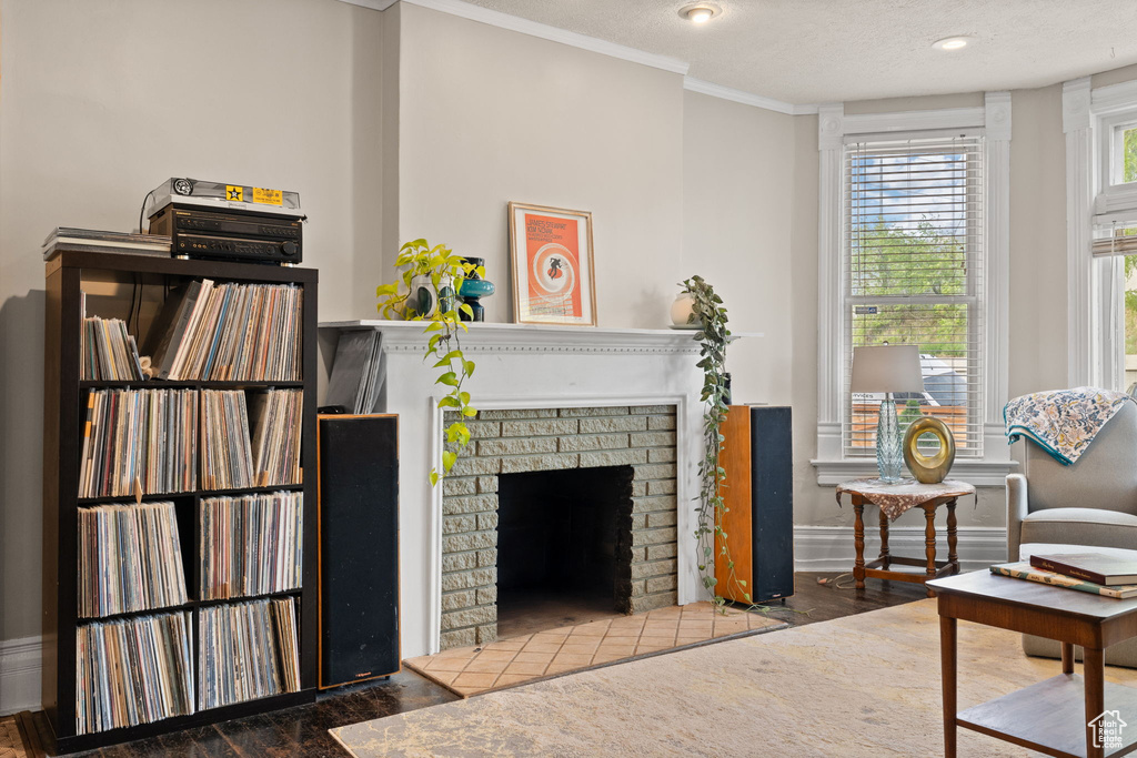 Living room with wood finished floors, ornamental molding, a brick fireplace, baseboards, and a textured ceiling