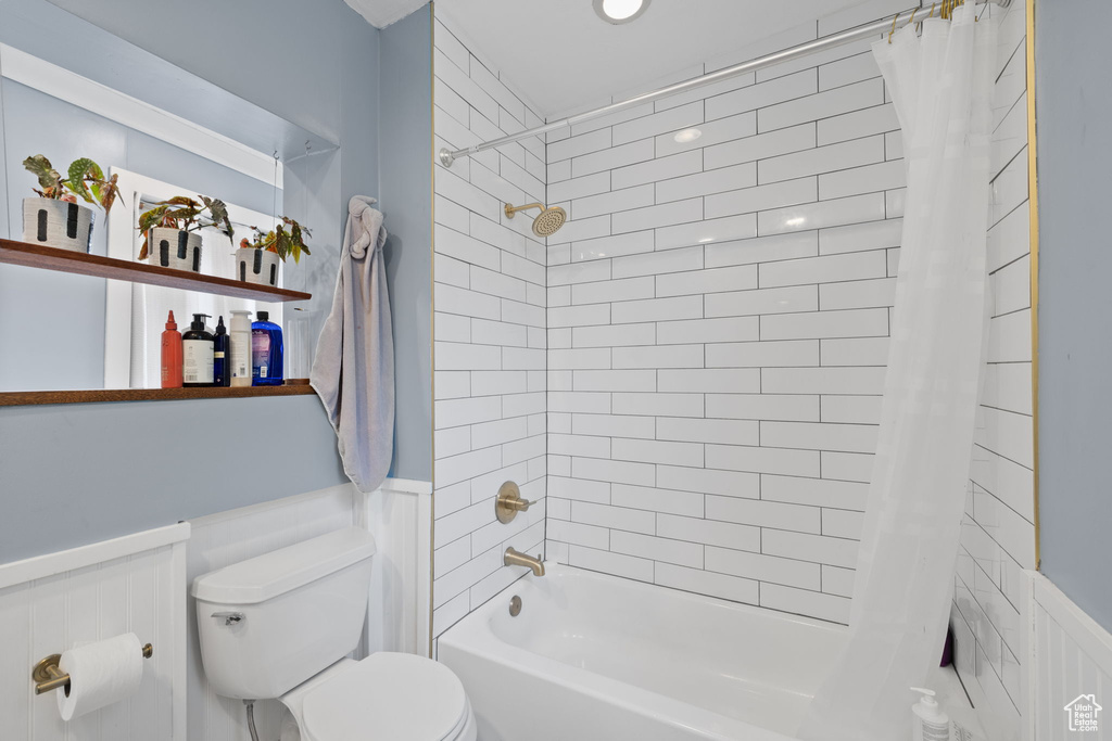 Full bathroom featuring a wainscoted wall, toilet, shower / tub combo with curtain, and a decorative wall