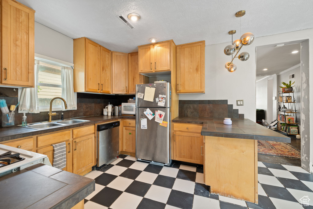 Kitchen featuring appliances with stainless steel finishes, light flooring, a sink, a peninsula, and hanging light fixtures