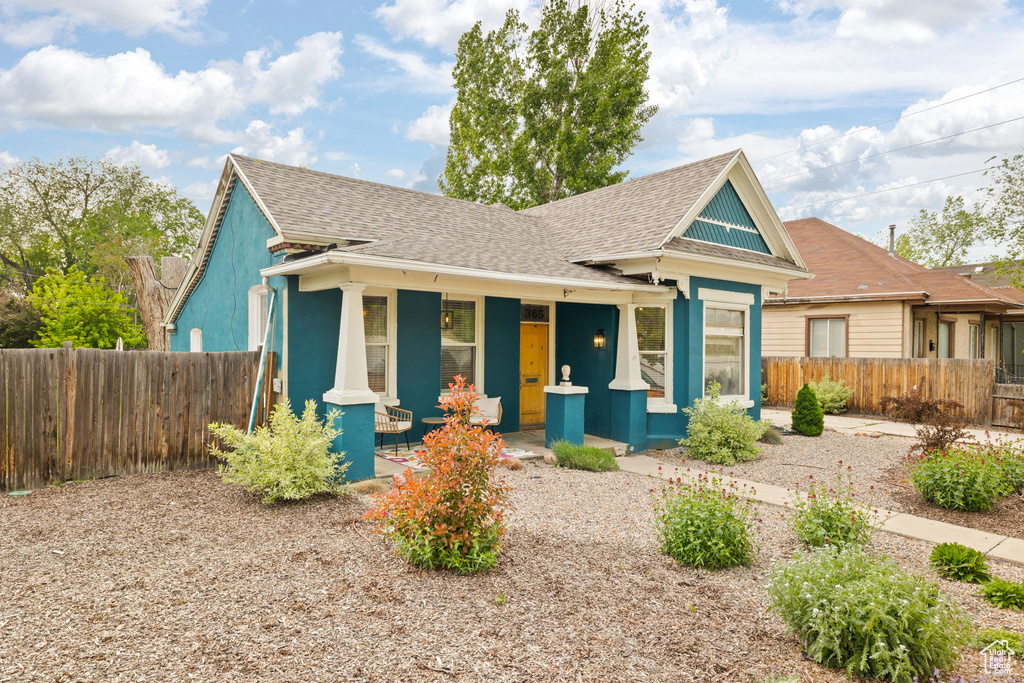 View of front of home with covered porch, roof with shingles, and fence