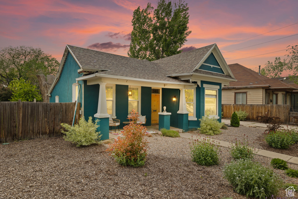 View of front of home with a porch, roof with shingles, and fence