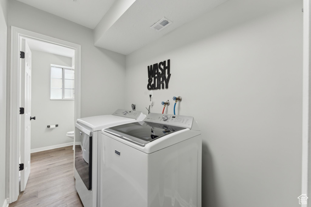 Laundry room with washing machine and clothes dryer, light wood-type flooring, and baseboards
