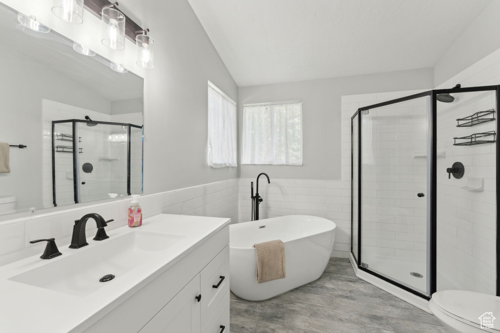 Bathroom featuring toilet, tile walls, a shower stall, a soaking tub, and vanity
