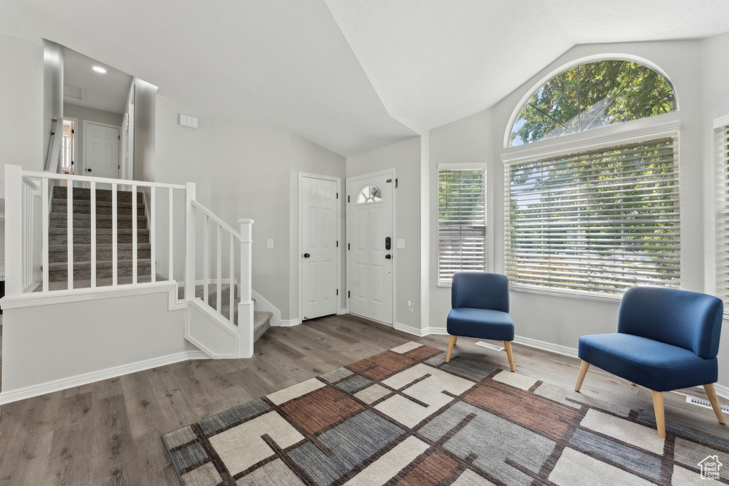 Living area with plenty of natural light, stairway, wood finished floors, and vaulted ceiling