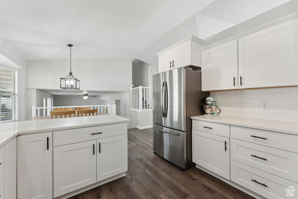 Kitchen featuring freestanding refrigerator, tasteful backsplash, white cabinets, dark wood-type flooring, and decorative light fixtures