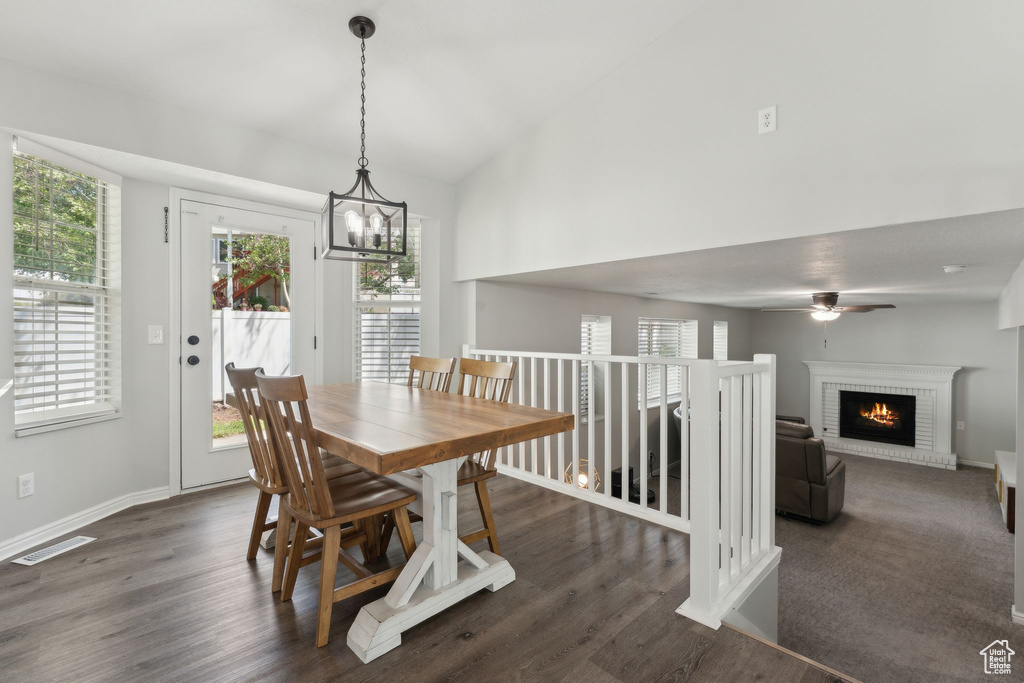 Dining space featuring dark wood finished floors, a fireplace, a ceiling fan, a chandelier, and vaulted ceiling