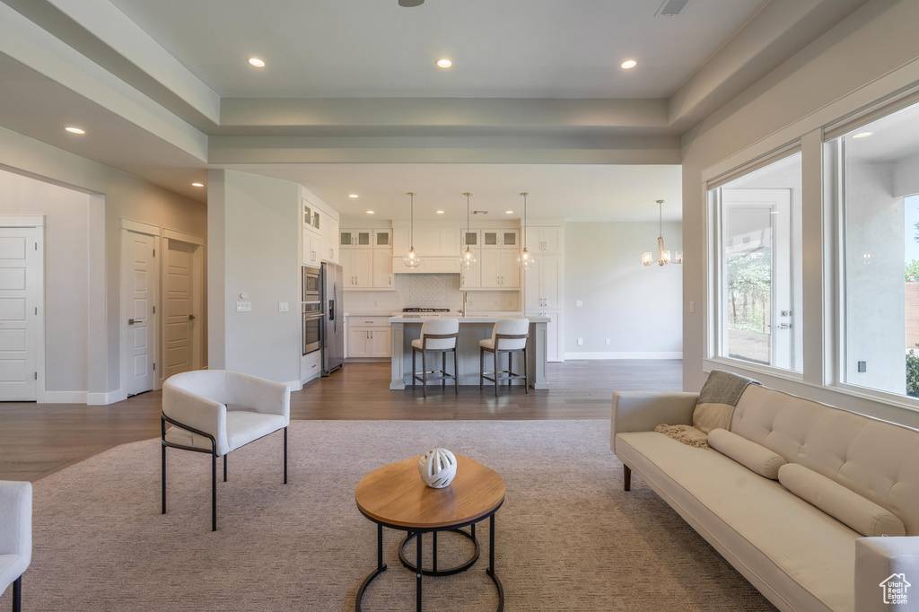 Living room with dark wood-style flooring, recessed lighting, a raised ceiling, a chandelier, and baseboards