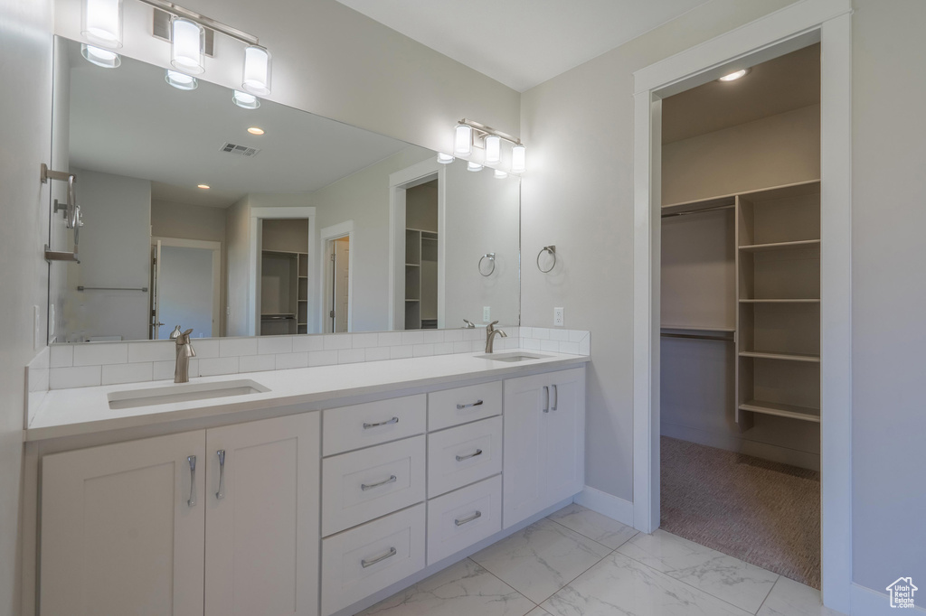 Bathroom featuring a walk in closet, marble look tile flooring, double vanity, baseboards, and recessed lighting