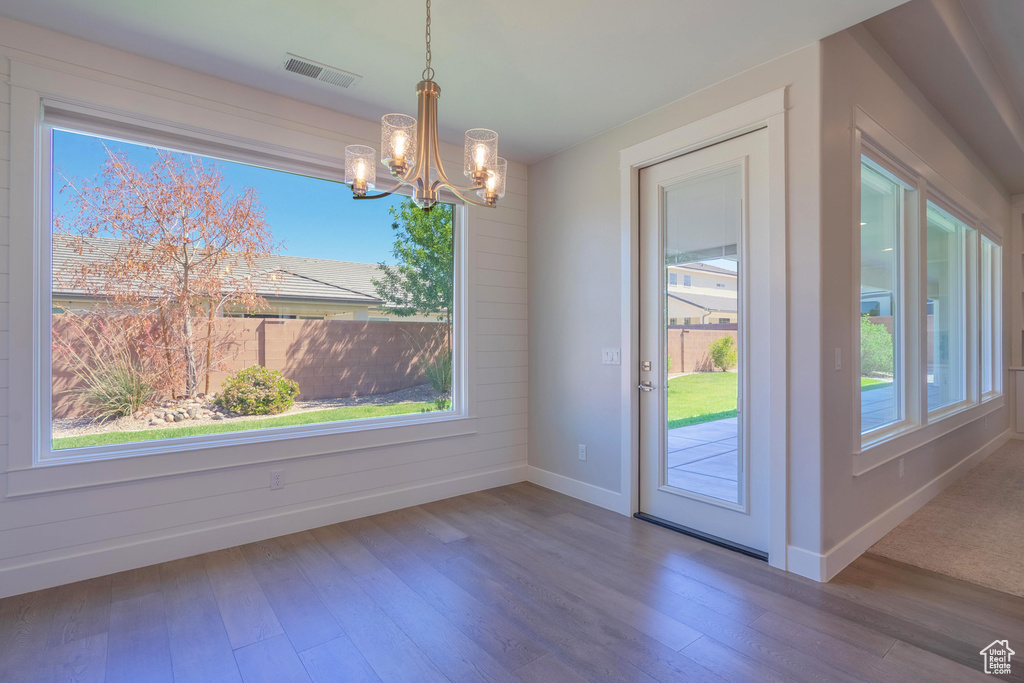 Unfurnished dining area featuring a chandelier, baseboards, wood-type flooring, and plenty of natural light