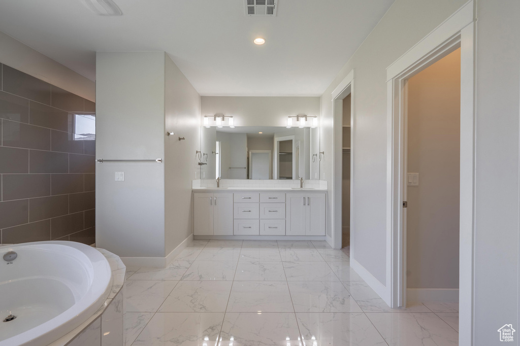 Bathroom featuring baseboards, a bath, double vanity, marble look tile flooring, and recessed lighting