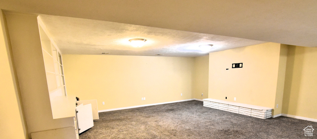 Finished below grade area featuring dark colored carpet and baseboards