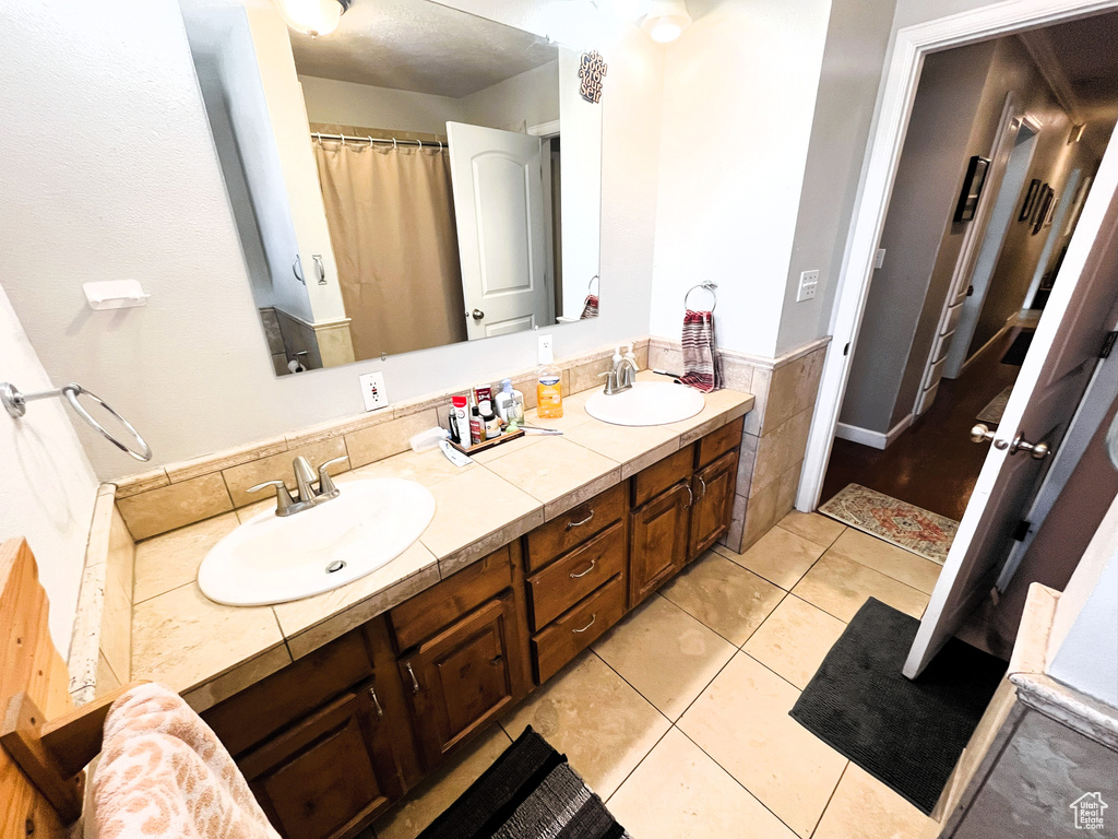 Bathroom featuring double vanity, a wainscoted wall, tile patterned flooring, and tile walls