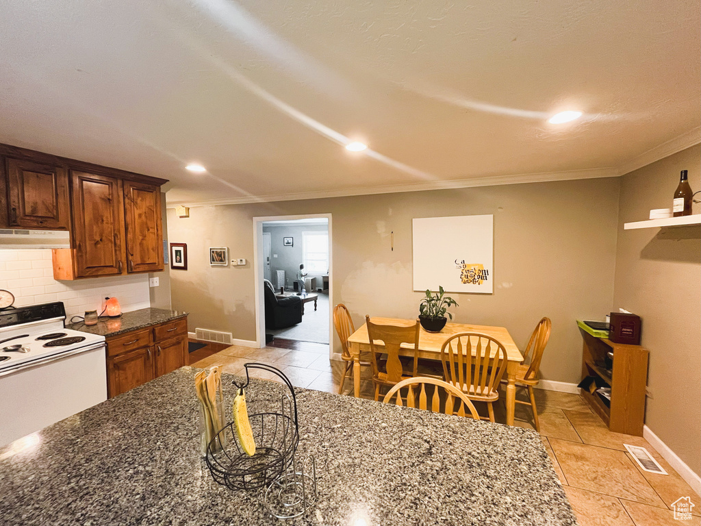 Kitchen with white range with electric cooktop, under cabinet range hood, ornamental molding, baseboards, and backsplash