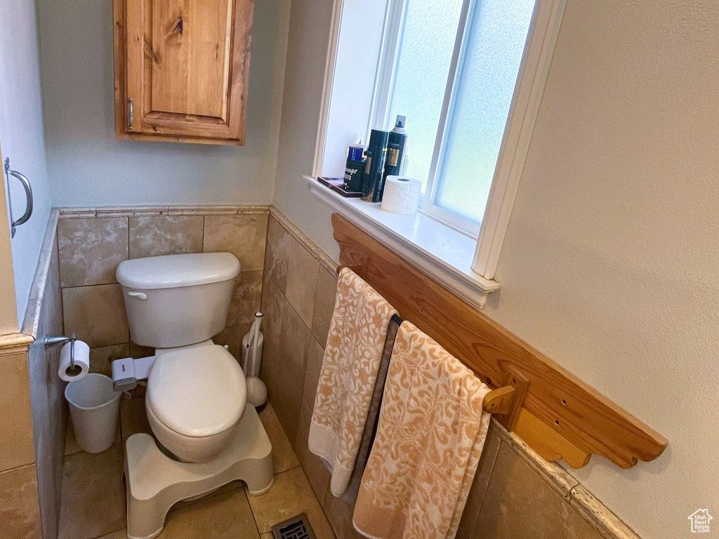 Bathroom with toilet, tile walls, tile patterned floors, and a wainscoted wall