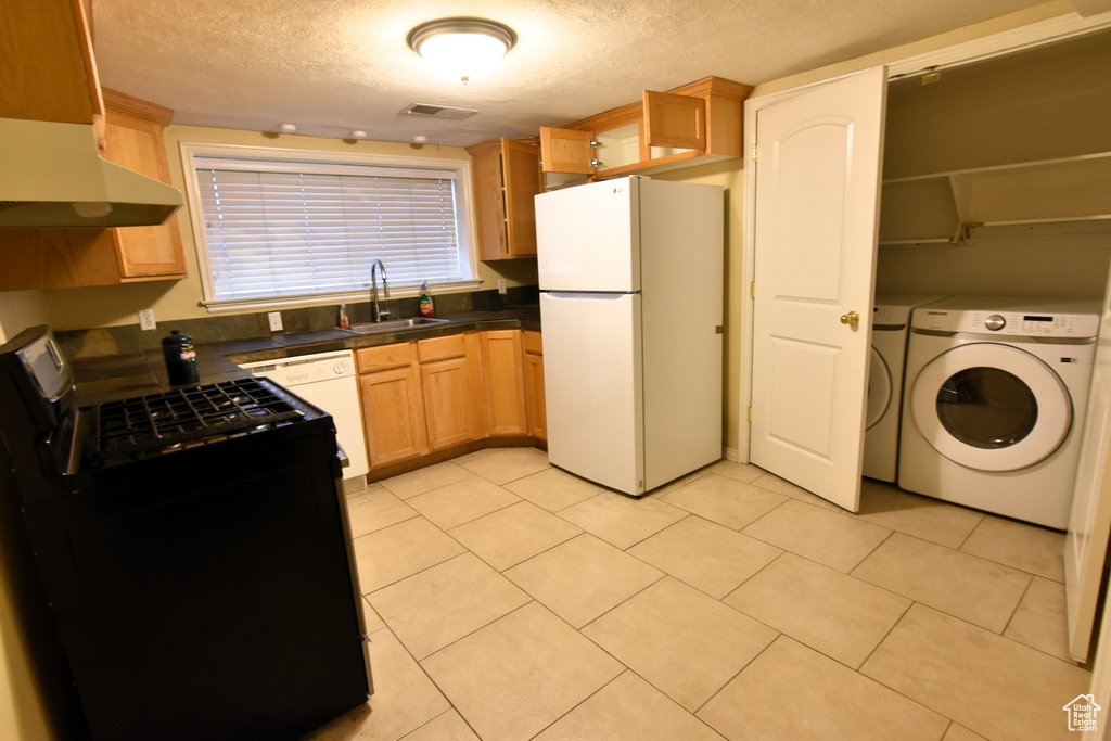 Kitchen with white appliances, a sink, separate washer and dryer, dark countertops, and under cabinet range hood