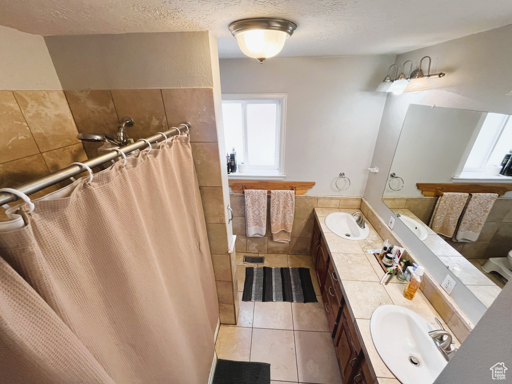 Bathroom with double vanity, a textured ceiling, a shower with curtain, tile patterned flooring, and tile walls