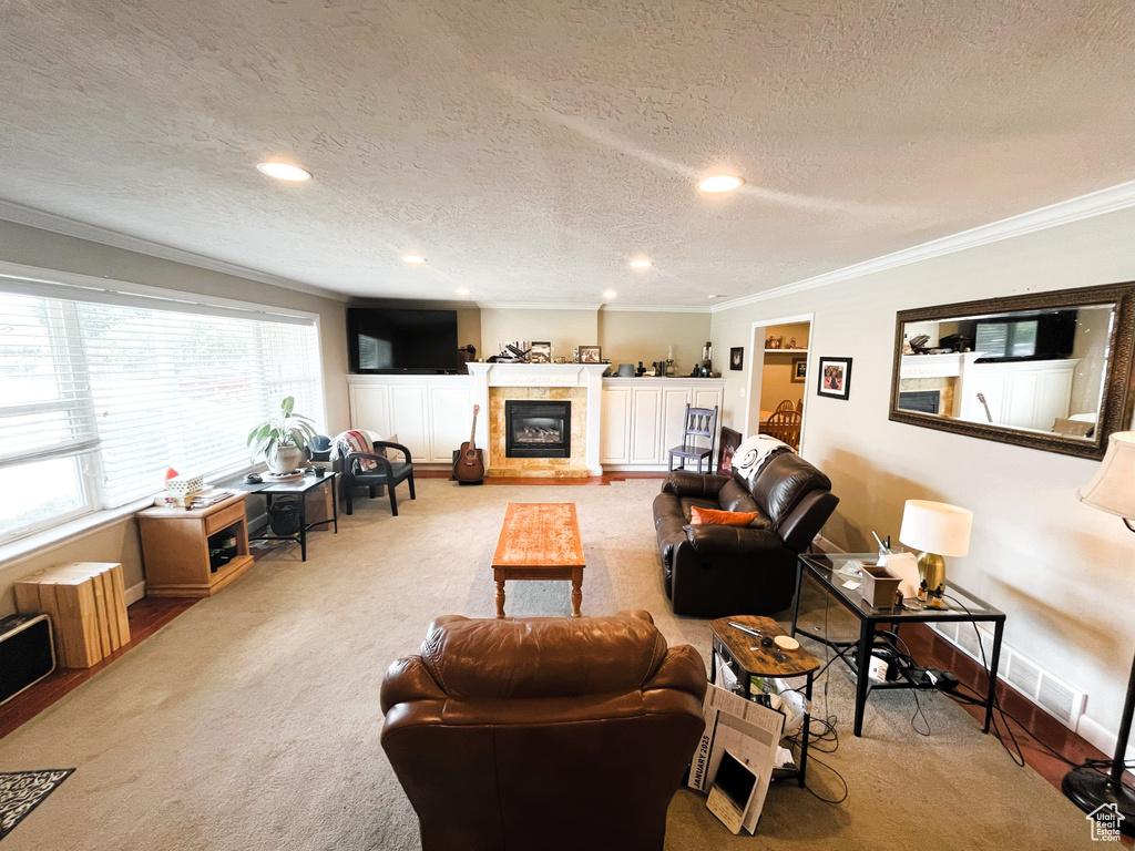 Carpeted living area featuring ornamental molding, a textured ceiling, a tiled fireplace, baseboards, and recessed lighting