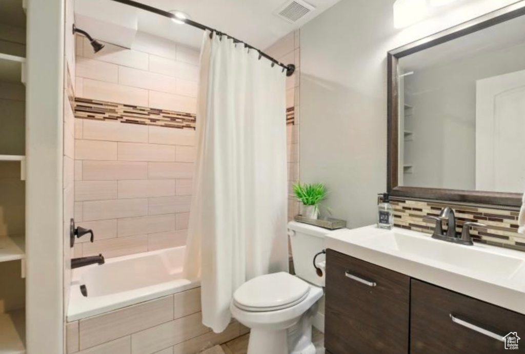 Full bath with toilet, decorative backsplash, vanity, and tiled shower / bath combo