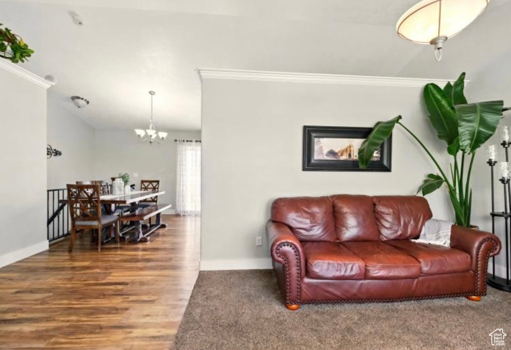 Living area with a chandelier, ornamental molding, baseboards, wood finished floors, and lofted ceiling