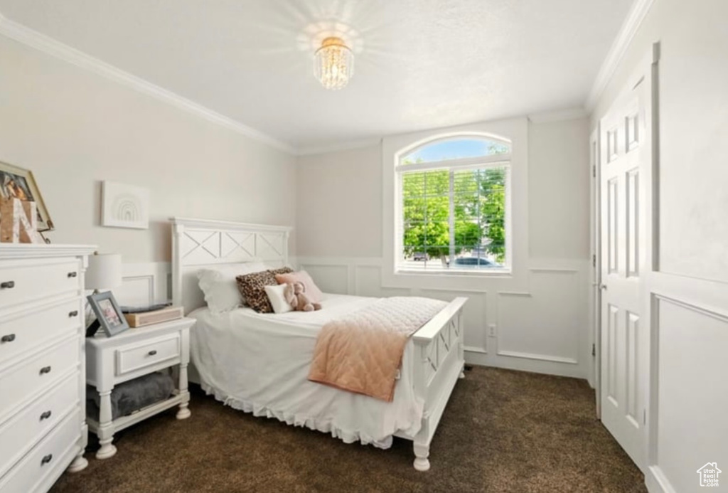 Bedroom with ornamental molding, dark carpet, a decorative wall, and a wainscoted wall
