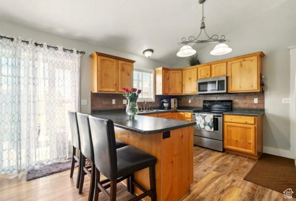 Kitchen with stainless steel appliances, decorative backsplash, dark countertops, and light wood finished floors