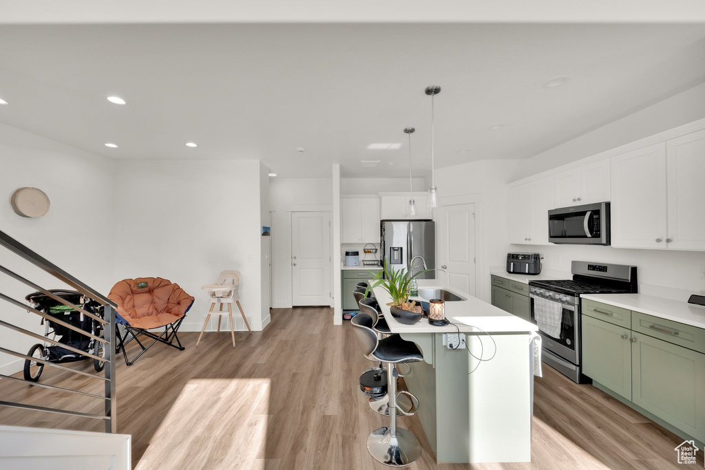 Kitchen with appliances with stainless steel finishes, green cabinets, a sink, light countertops, and light wood-type flooring