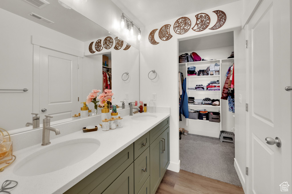 Bathroom with double vanity, a walk in closet, and wood finished floors